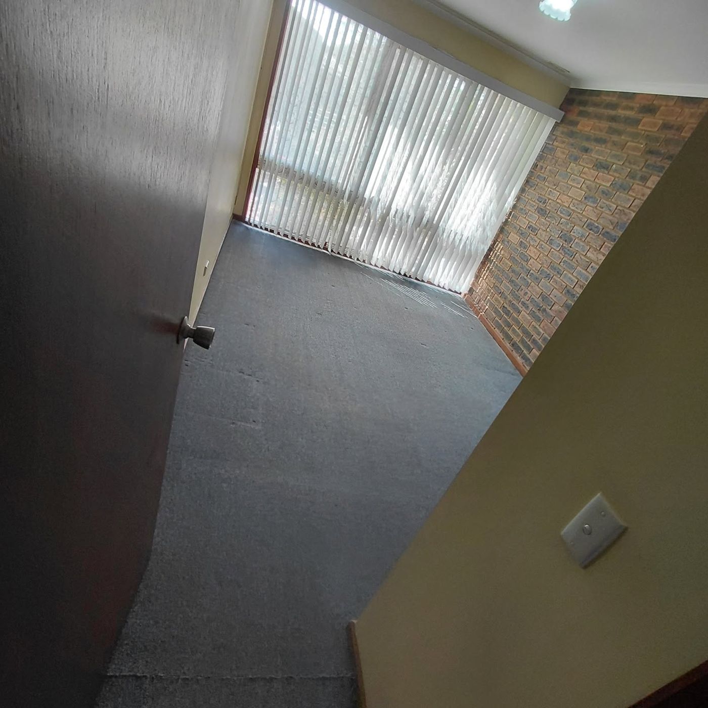 An empty rental room with cleaned dark carpet and vertical blinds